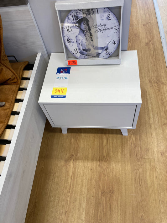 Biały stolik nocny z szufladą na efektownych białych nóżkach.