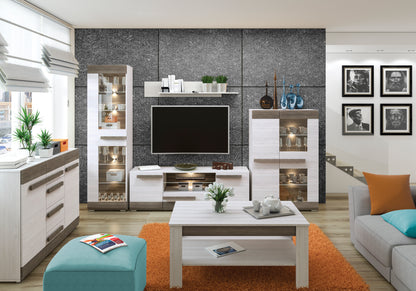 Zdjęcie przedstawiające przykładową aranżację nowoczesnego salonu z meblami Blanka. Na zdjęciu widoczna komoda z szufladami, dwie witryny z podświetleniem LED, stolik kawowy, nowoczesna szafka RTV oraz półka wisząca.