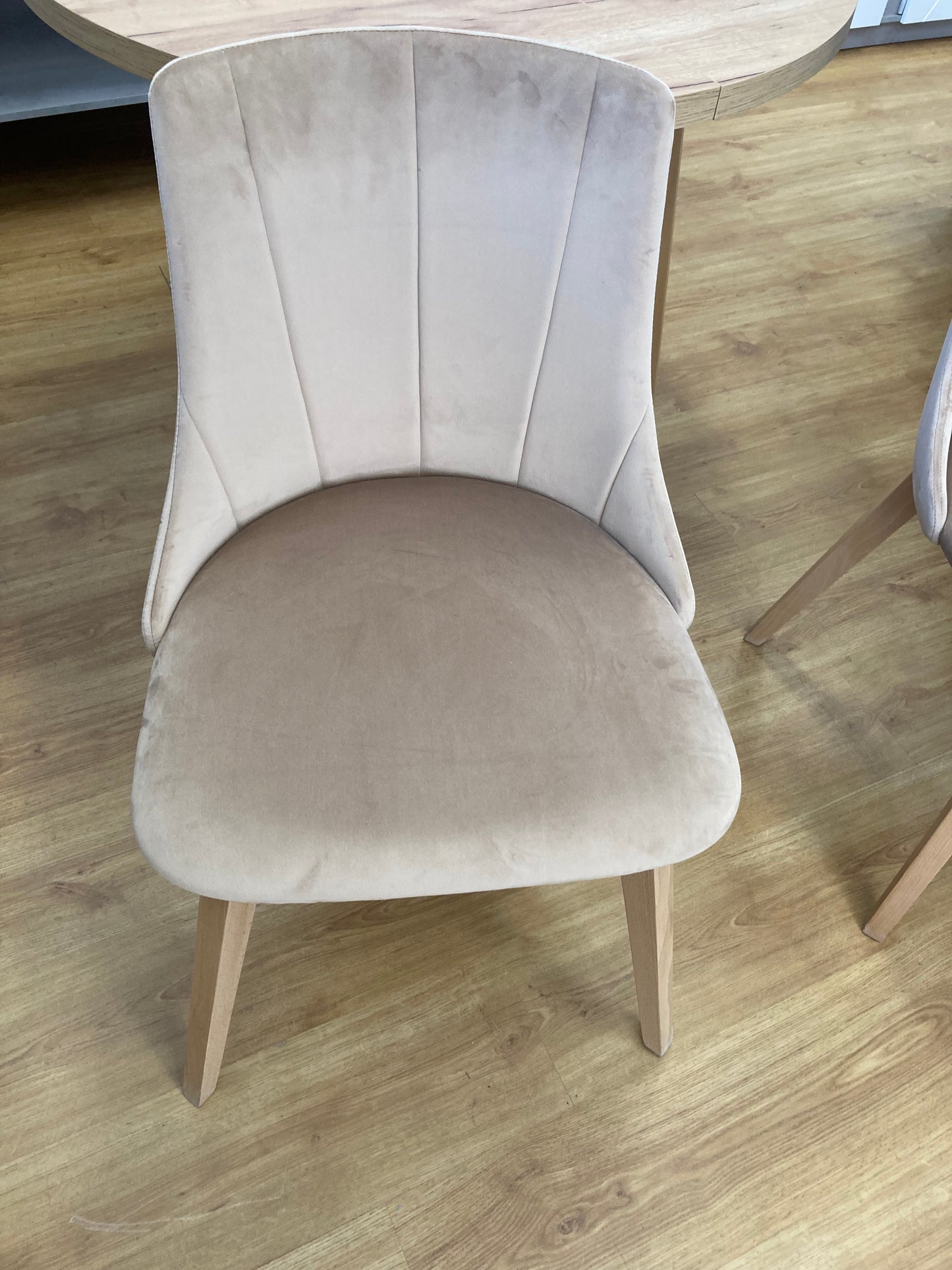 Krzesło KT-61 w jasnej tkaninie z ozdobnymi przeszyciami na oparciu, gładkim obszernym i wygodnym siedziskiem oraz drewnianymi jasnymi nogami.